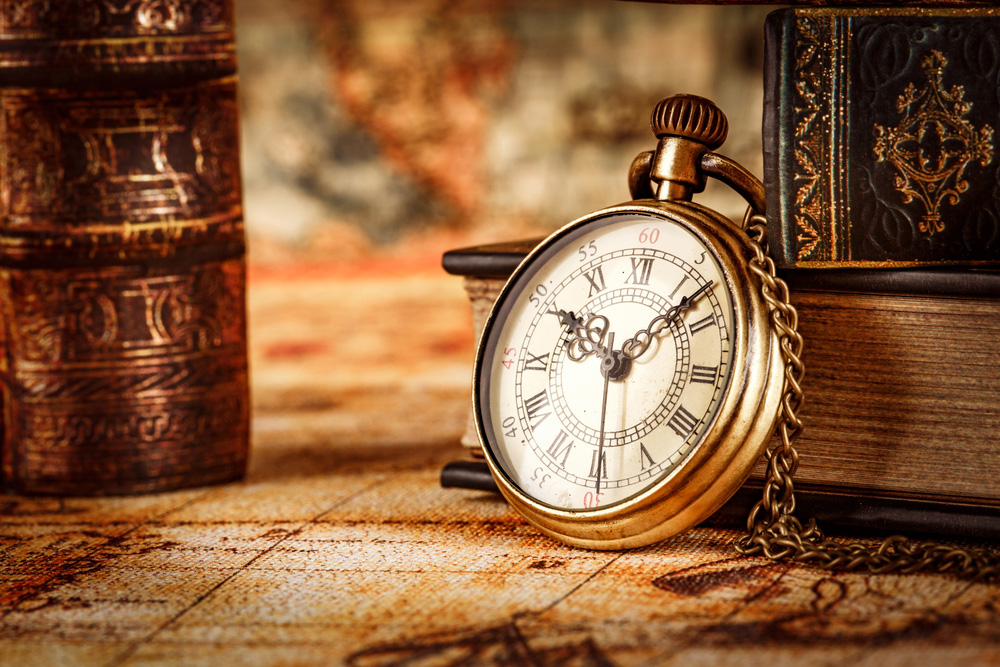 Eski kitapların önünde duran bir saat görüntüsü. Lakin antika saatte diyebiliriz..